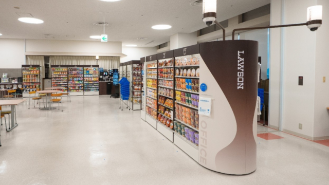 مشهد متجر مؤتمت داخل مقر Kyocera مع شاشة دفع ذاتي وتطبيق هاتف يظهر شعارات Lawson وKDDI وKyocera.