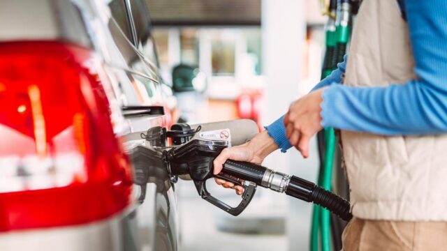أحد محطات الوقود البريطانية أمامها لوحة أسعار الوقود وسائق يقف بجانب سيارته